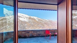 A balcony with a stone wall, a red chair, and a view of snow-covered mountains. - 100m from ski slopes, floor -1, swimming pool, terrace, tv, ski locker, 32m², Les Menuires (Les Menuires)