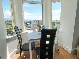 Una habitación con un amplio ventanal que ofrece vista al mar y a las casas, una mesa con sillas y un florero con adornos.