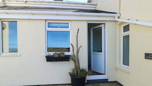 A building with a white exterior, a window with a view, a door, and a potted plant. - Ewyn Y Don (Holyhead)