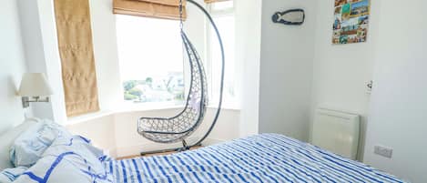 Un dormitorio con una hamaca colgante, una cama con ropa de cama a rayas, una ventana con vistas y una pared decorada con un motivo de pez.