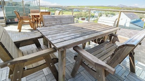 A wooden deck with a table and chairs, overlooking a landscape with buildings and hills. - Ewyn Y Don (Holyhead)