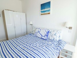 A bedroom with a bed, a wardrobe, two bedside lamps, and a painting of a beach scene.