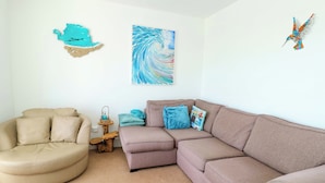 A living room with a beige armchair, a brown sofa, and a small wooden side table with a basket and decorative items. - Ewyn Y Don (Holyhead)