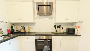 A kitchen with white cabinets, a stainless steel oven, a kettle, and a toaster. - Ewyn Y Don (Holyhead)
