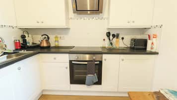 Una cocina con armarios blancos, horno de acero inoxidable, tetera y tostadora.