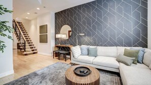 A modern living room with a staircase, a sofa, a coffee table, and a geometric-patterned wall. - Big and Beautiful 5BR Triplex in Shaw/Bloomingdale (Washington)