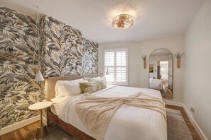 Ein Schlafzimmer mit einem großen Bett, einem Wandspiegel, einer Deckenleuchte und einem Fenster mit Jalousien.