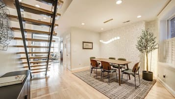 Ein modernes Interieur mit einer Holztreppe, einer Essecke mit Tisch und Stühlen sowie einer Wand mit Muster.