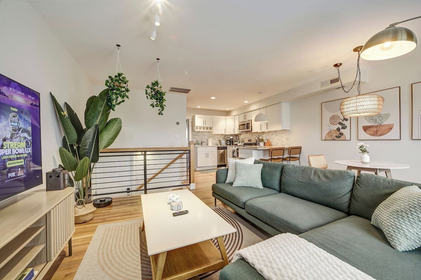 Ein modernes Wohnzimmer mit einer Couch, einem Couchtisch und einem Fernseher. Im Hintergrund ist eine Küche mit Schränken und einem Essbereich zu sehen.