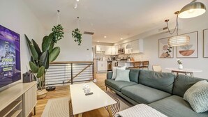 A modern living room with a sofa, coffee table, and a TV. There is a kitchen in the background with cabinets and a dining area. - Big and Beautiful 5BR Triplex in Shaw/Bloomingdale (Washington)
