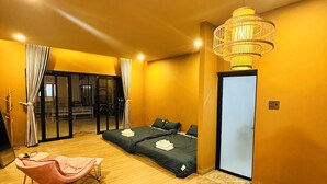 Habitación de hotel moderna con piso de madera, dos camas, una mecedora, un ventanal grande y una lámpara colgante.