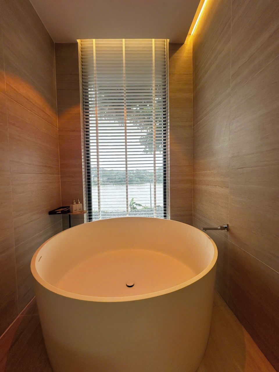 A modern bathroom with a large bathtub, wooden walls, and a window with blinds.
