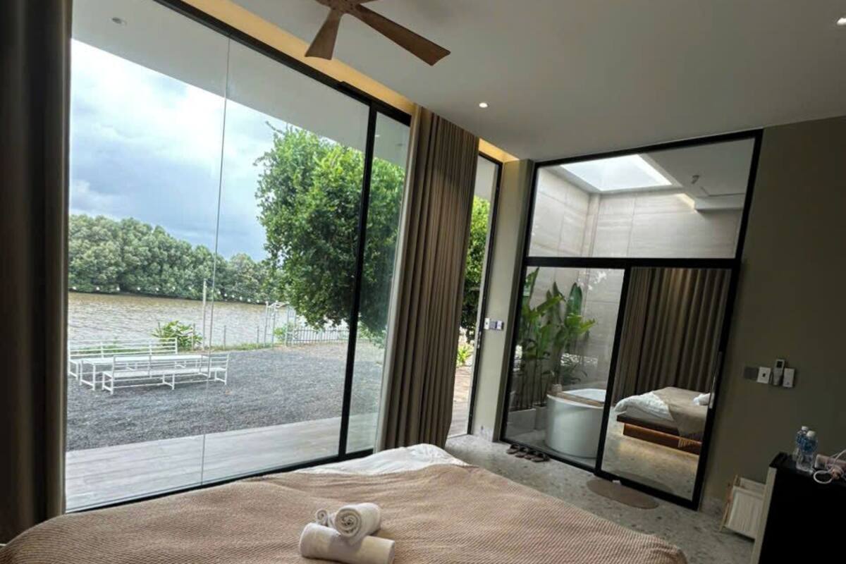 A modern bedroom with a large bed, a ceiling fan, and a view of a pool and outdoor seating.
