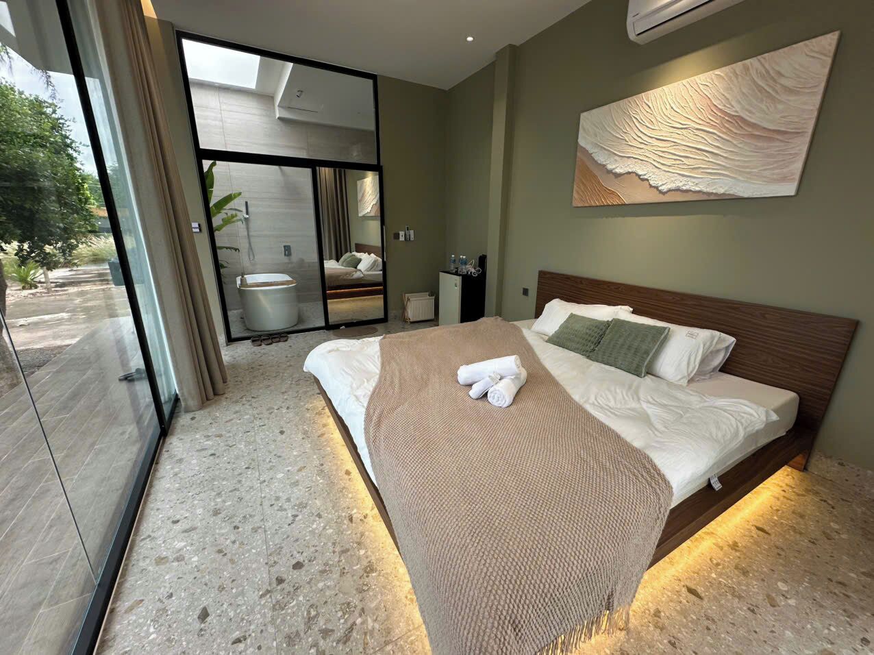 A modern hotel room with a large bed, a glass door leading to a balcony, and a wall-mounted artwork.