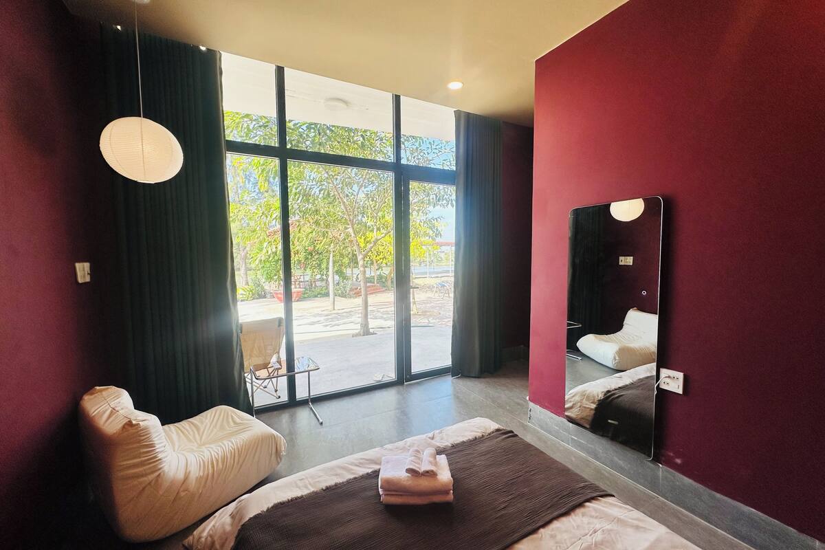 A modern hotel room with a large bed, a chair, a mirror, and a view of the outdoors.