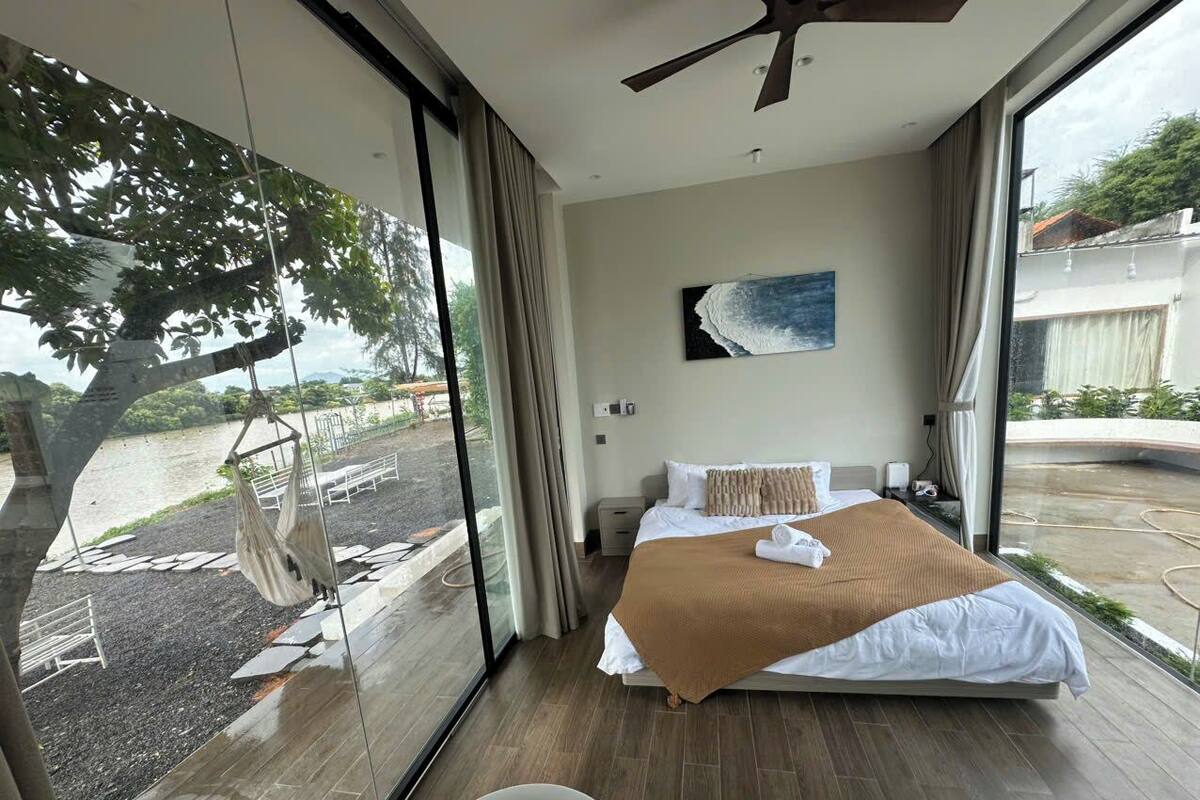 A modern hotel room with a large bed, a ceiling fan, and a view of the outdoors.