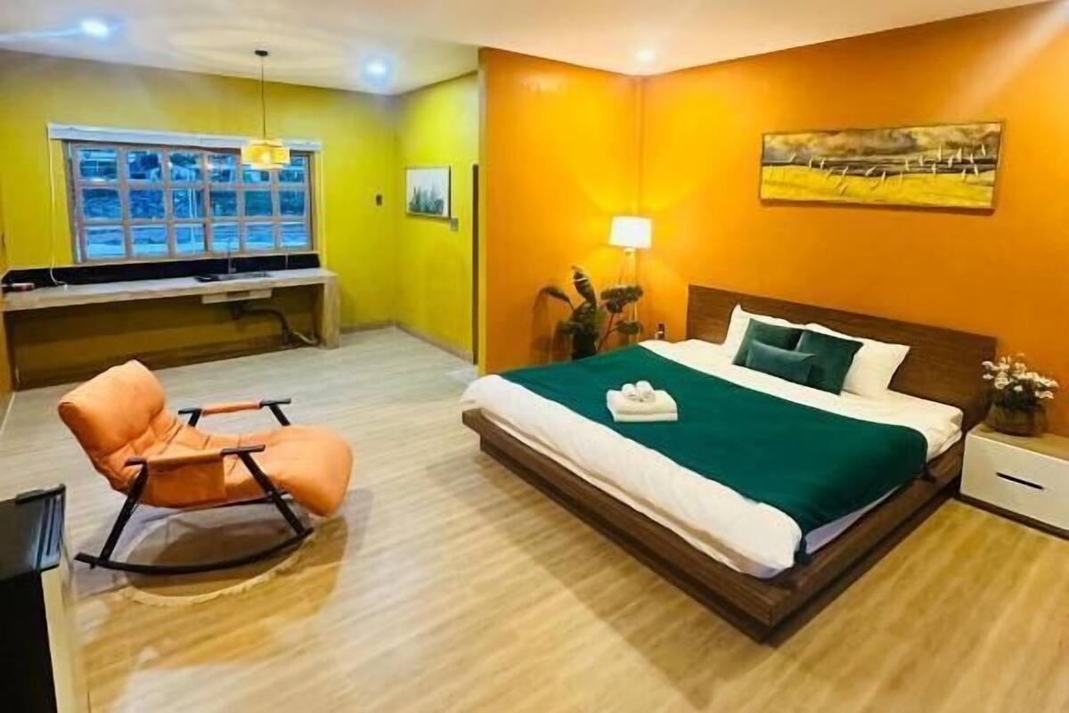 A hotel room with a bed, a rocking chair, a desk, and a window.
