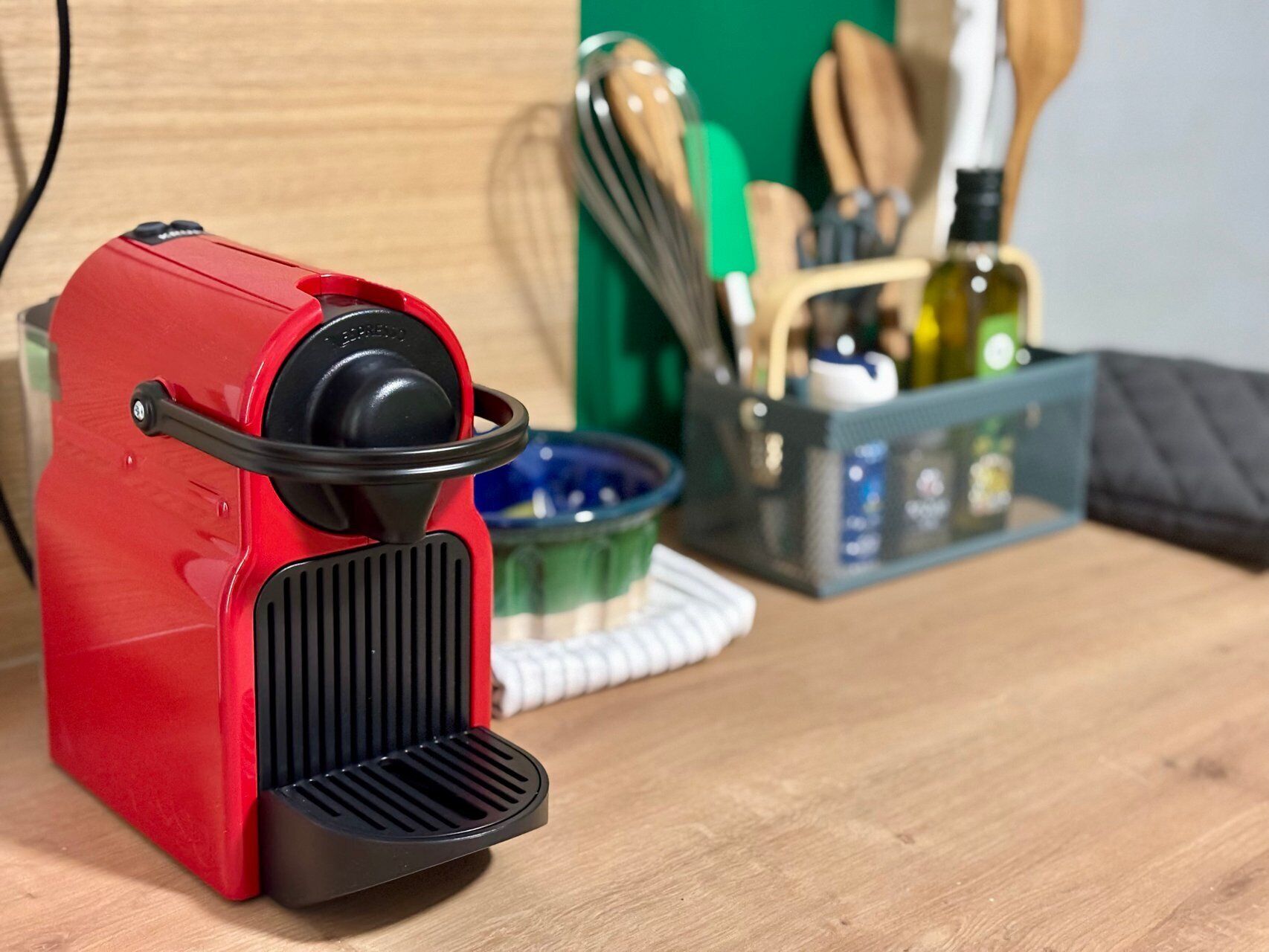 Une machine à expresso rouge est posée sur une surface en bois, avec des ustensiles de cuisine et un bol bleu en arrière-plan.