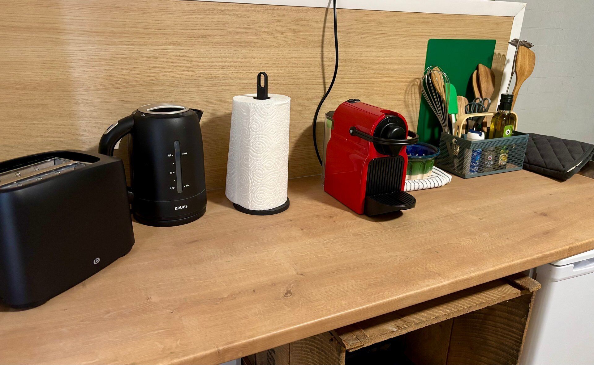 A kitchen counter with a coffee maker, a toaster, a paper towel holder, a red electric kettle, and kitchen utensils.