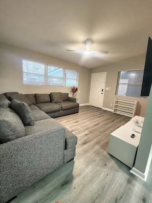 Ein Wohnzimmer mit einer Eckcouch, einem weißen Couchtisch und einer Tür mit Fenster.
