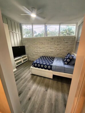 Ein Schlafzimmer mit einem Bett, einem Fernseher, einem Deckenventilator und einer Ziegelwand.