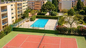 Een tennisbaan met een zwembad, omringd door groen en gebouwen.