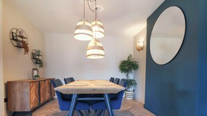 A dining area with a wooden table, blue chairs, hanging pendant lights, a potted plant, and a decorative mirror. - Falcon Luxe (Whitby)