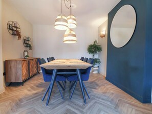 A dining area with a wooden table, blue chairs, hanging pendant lights, a potted plant, and a decorative mirror. - Falcon Luxe (Whitby)