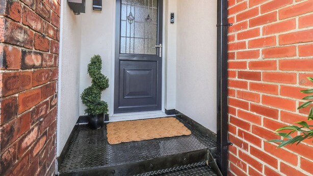 A black door with a glass panel, a small potted plant, and a doormat. - Falcon Luxe (Whitby)