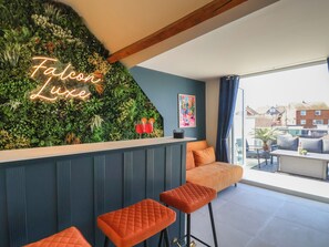 Eine Bar mit einer Neonreklame, einer grünen Wand mit Pflanzen und Blick auf Gebäude im Hintergrund.