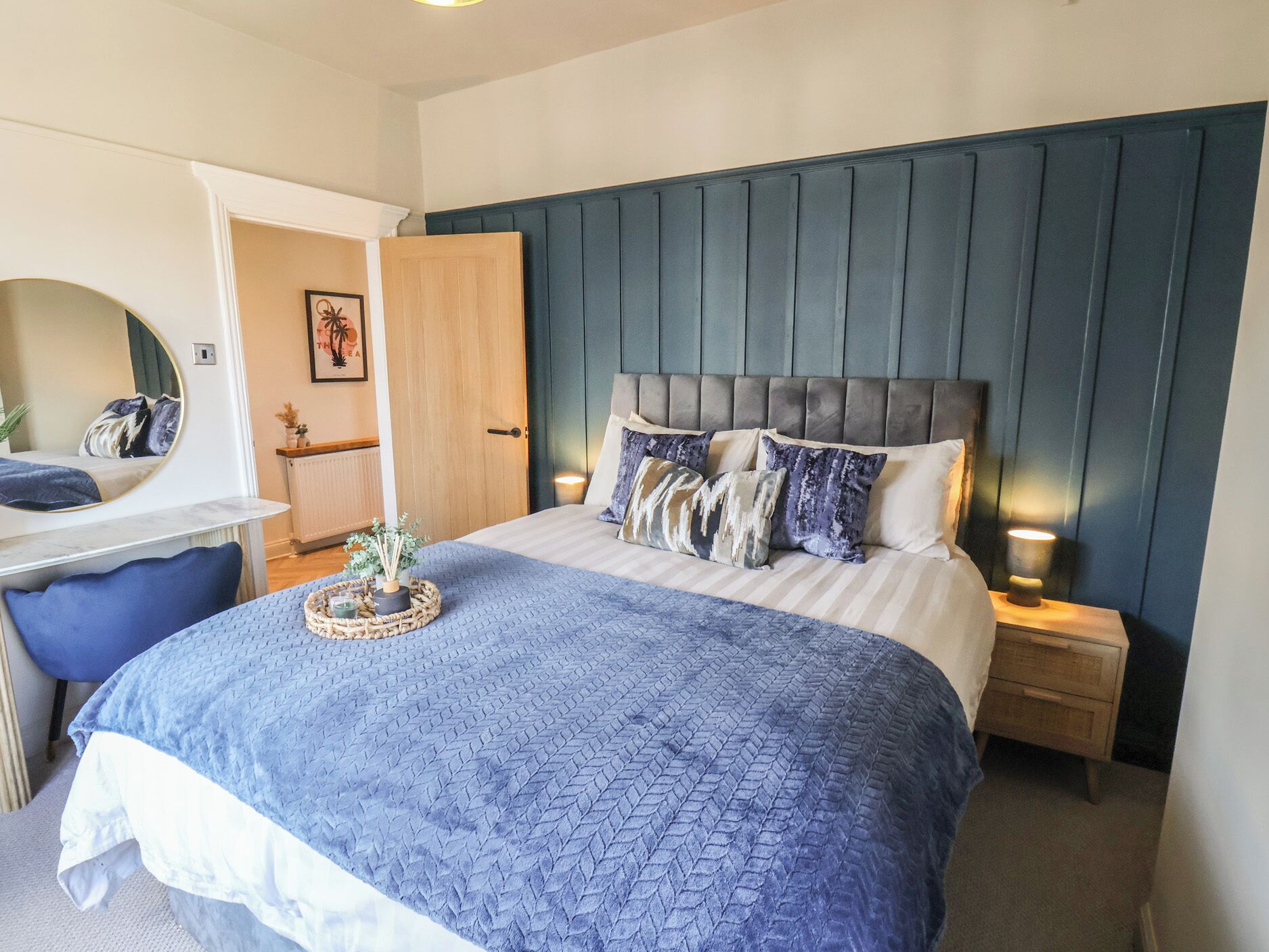 Une chambre à coucher avec un lit, des tables de chevet, une commode, un miroir et une porte.