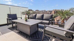 A rooftop terrace with a grey sofa, two chairs, a small table, and a potted plant. - Falcon Luxe (Whitby)