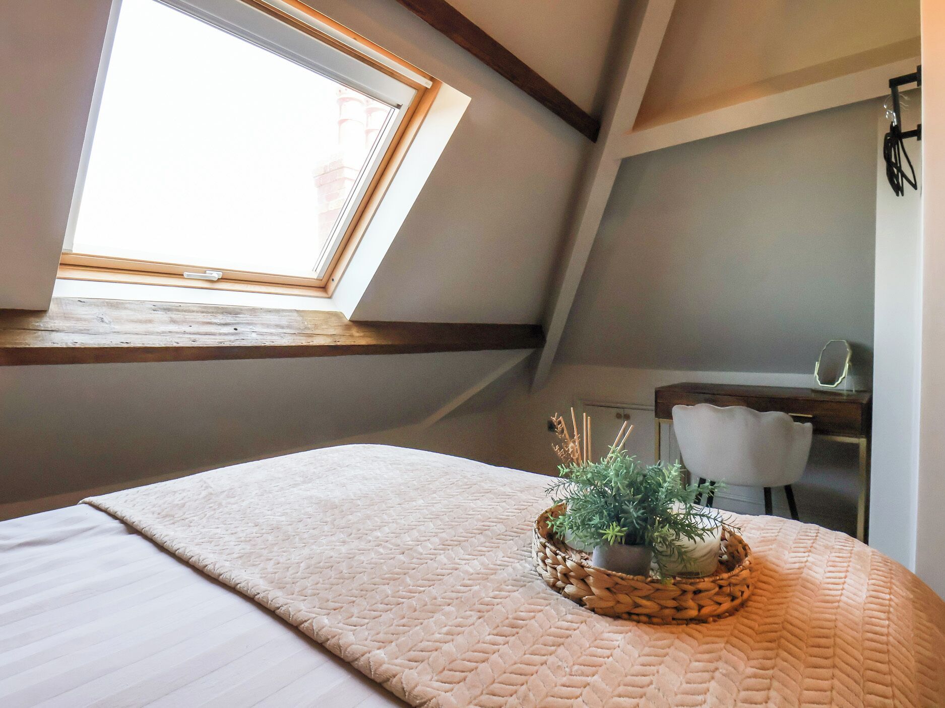A bedroom with a skylight, a bed with a textured blanket, a small desk, and a potted plant.