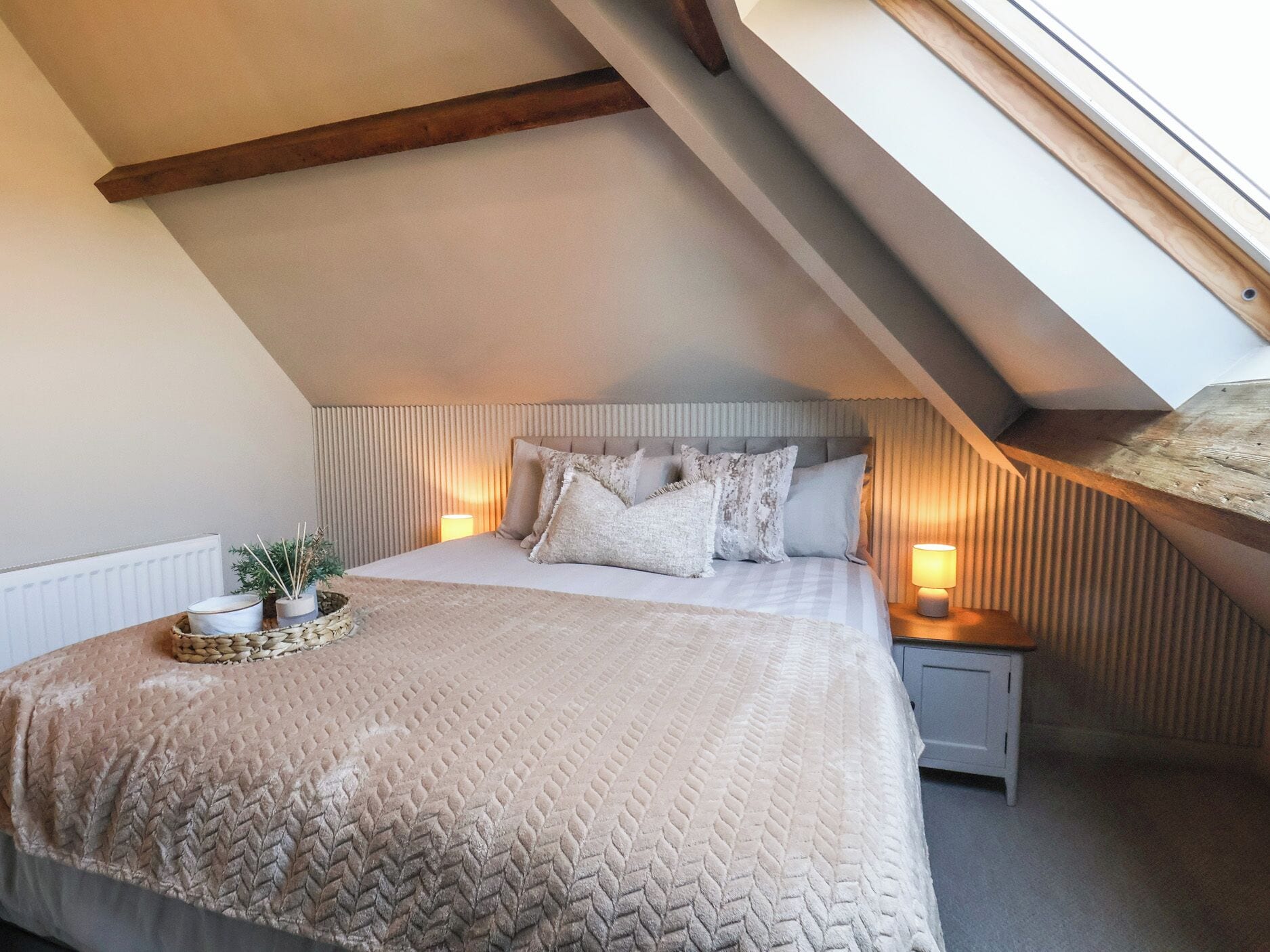 A bedroom with a sloped ceiling, a bed with a textured blanket, two bedside lamps, and a small plant on the nightstand.