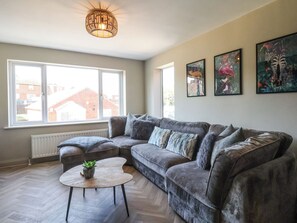A modern living room with a sectional sofa, a round coffee table, and a large window providing a view of the outside. - Falcon Luxe (Whitby)