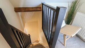 A staircase with wooden railings, carpeted steps, and a small table with a woven seat. - Falcon Luxe (Whitby)