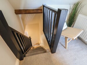 A staircase with wooden railings, carpeted steps, and a small table with a woven seat. - Falcon Luxe (Whitby)