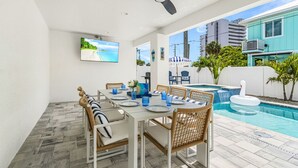 Zona pranzo con piscina, mobili da esterno e televisione a parete.