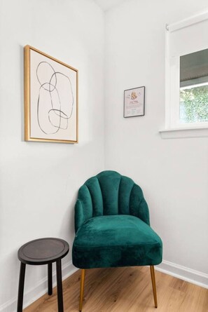 A corner room with a teal velvet armchair, a small round stool, and two framed artworks on the wall. - The Lyric - Every Stay Hits the Right Note (Nashville)