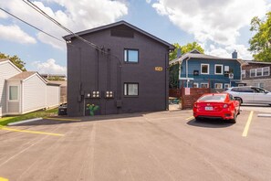 Een gebouw met twee verdiepingen, een donkere gevel en het nummer '1023' dat duidelijk zichtbaar is. Er bevindt zich een parkeerplaats voor het gebouw, waar een rode auto geparkeerd staat.