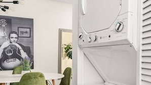 A modern kitchen with white appliances, a dining area with green chairs, and a wall-mounted guitar poster. - The Lyric - Every Stay Hits the Right Note (Nashville)