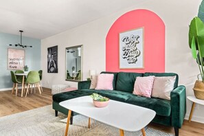 Ein modernes Wohnzimmer mit einem grünen Sofa, einem weißen Couchtisch und einer Wand in Pink.