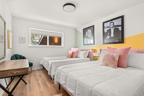 Quarto de hotel com duas camas, uma escrivaninha e uma janela.