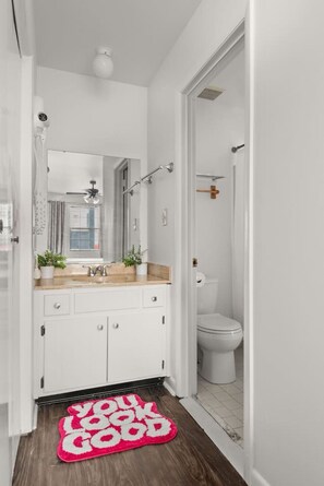 Ein schmaler Flur mit einer Badezimmertür, einem weißen Waschbecken mit Spiegel und einem rosa Teppich.