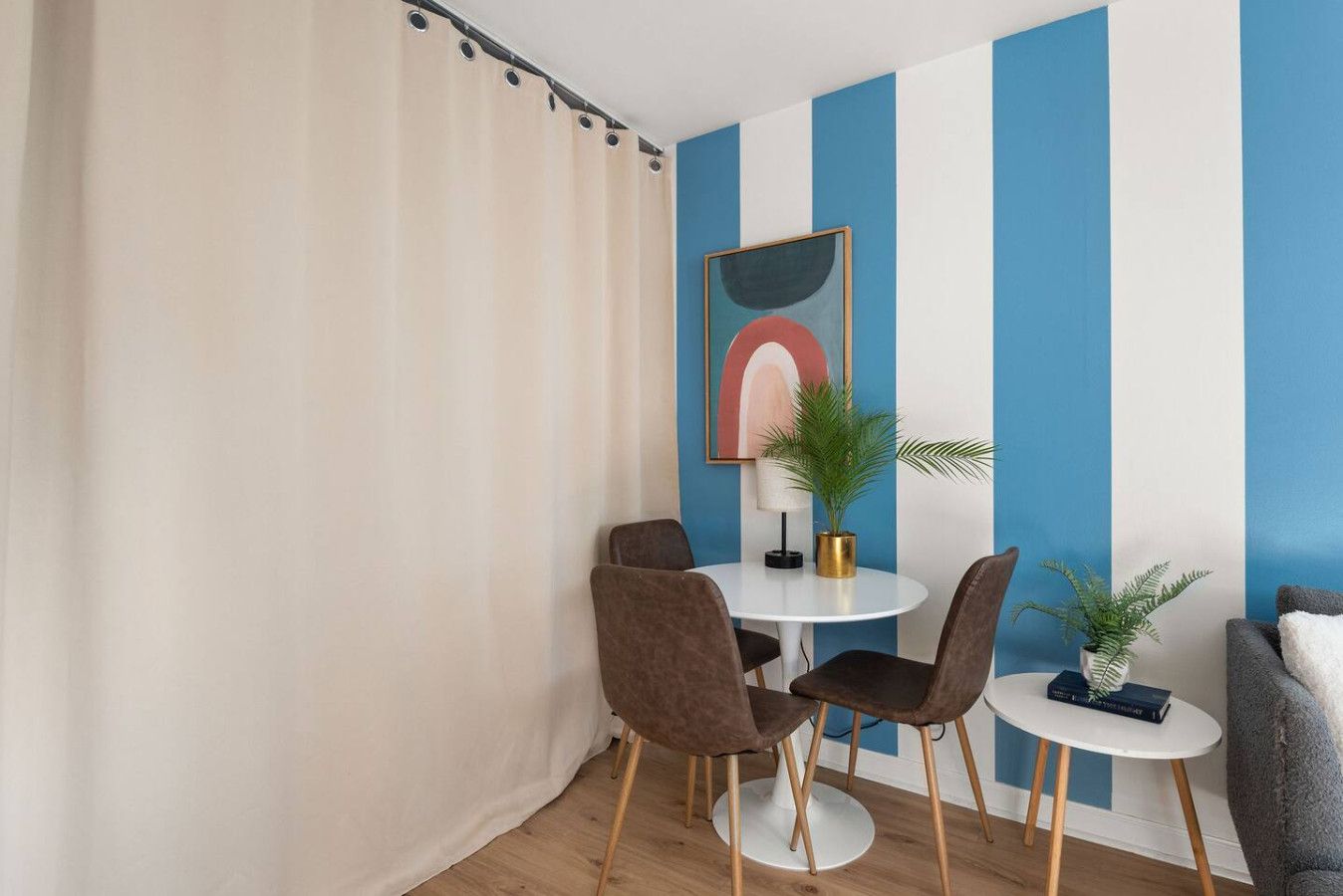 Ein Zimmer mit rautenmusterter Wand, einem runden Tisch mit Stühlen, einer Zimmerpflanze und einem gerahmten Kunstwerk.