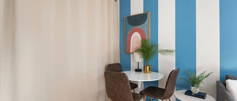 Ein Zimmer mit rautenmusterter Wand, einem runden Tisch mit Stühlen, einer Zimmerpflanze und einem gerahmten Kunstwerk.