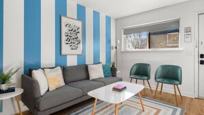 Ein Wohnzimmer mit grauem Sofa, zwei grünen Sesseln, einem weißen Couchtisch und einem Streifen Teppich.