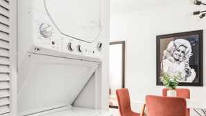 Una cucina moderna con lavatrice e asciugatrice integrate, una zona pranzo con sedie rosse e un quadro appeso al muro.