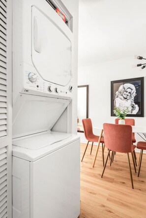 A modern kitchen with a built-in washer and dryer, a dining area with red chairs, and a framed artwork on the wall. - The Lyric - Your Backstage Pass to Nashville (Nashville)