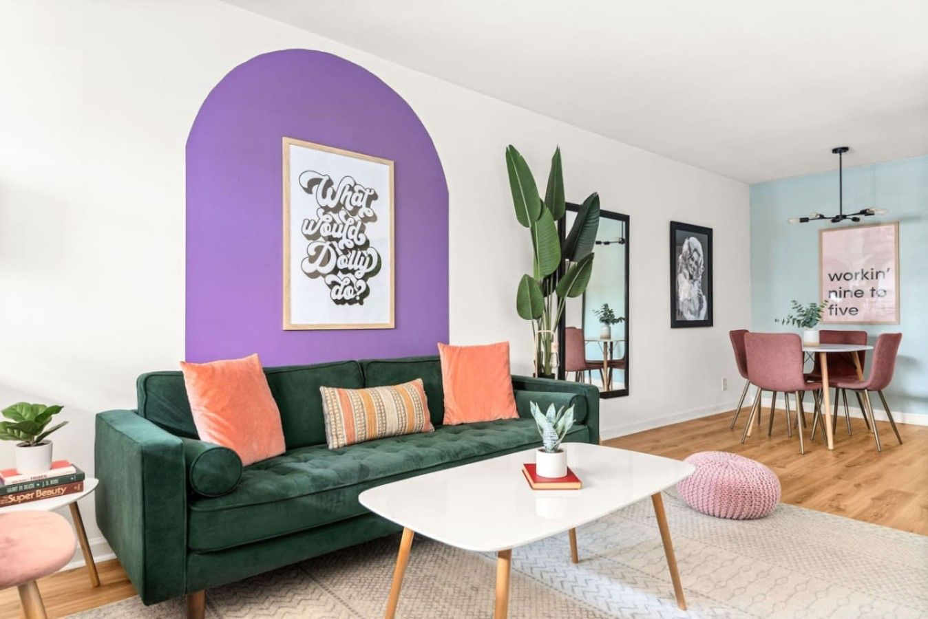 A living room with a green sofa, a white coffee table, and a purple accent wall.